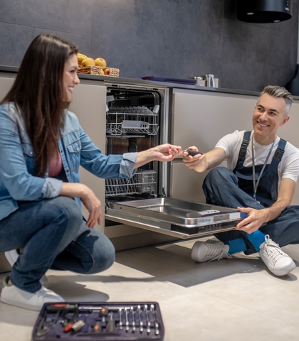 woman holding out tool to plumbing near dishwasher